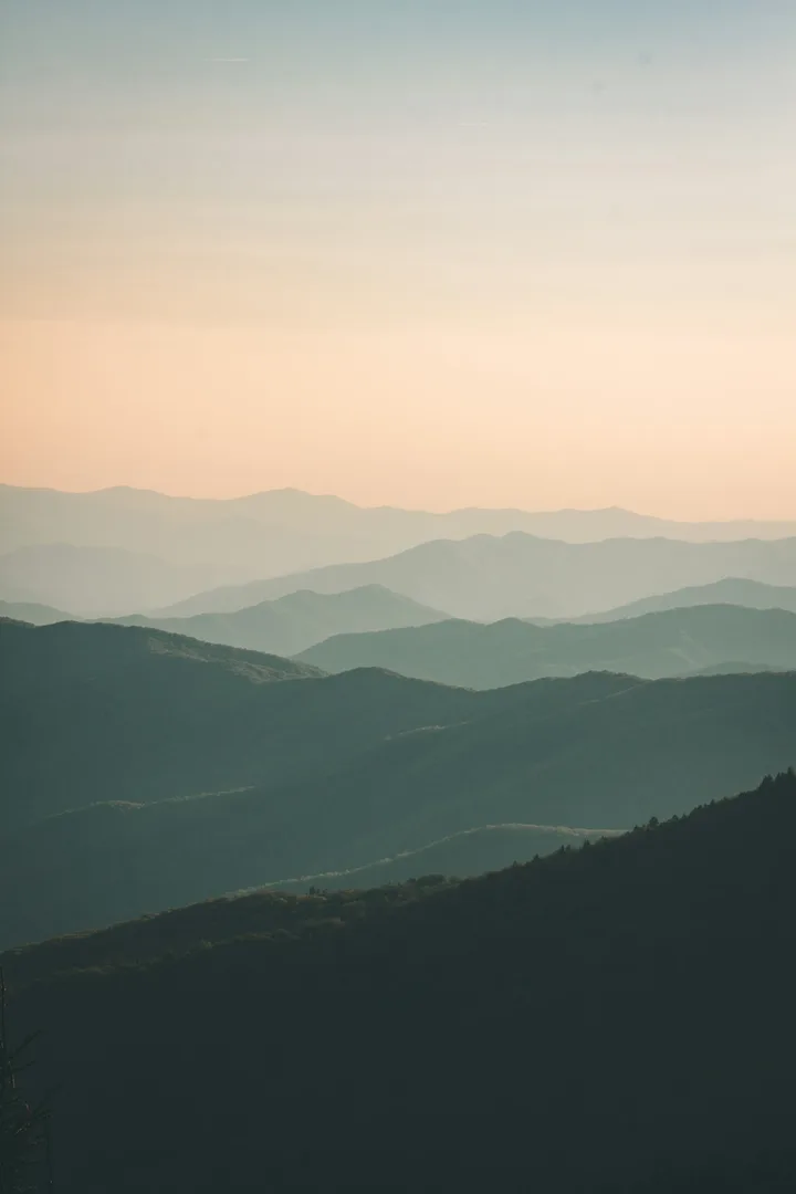 Creste di montagna sfumate una dietro l'altra nella foschia al tramonto.