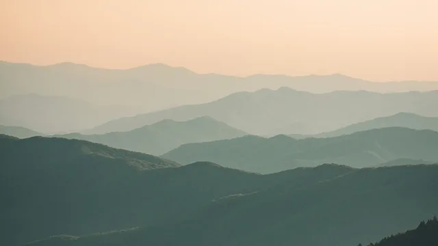 Creste di montagna sfumate una dietro l'altra nella foschia al tramonto.